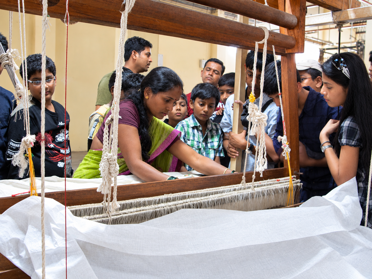 Students watching a weaver work a handloom on a field visit