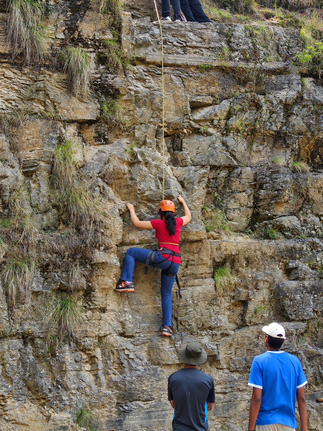 A student rock climbing with instructors belaying