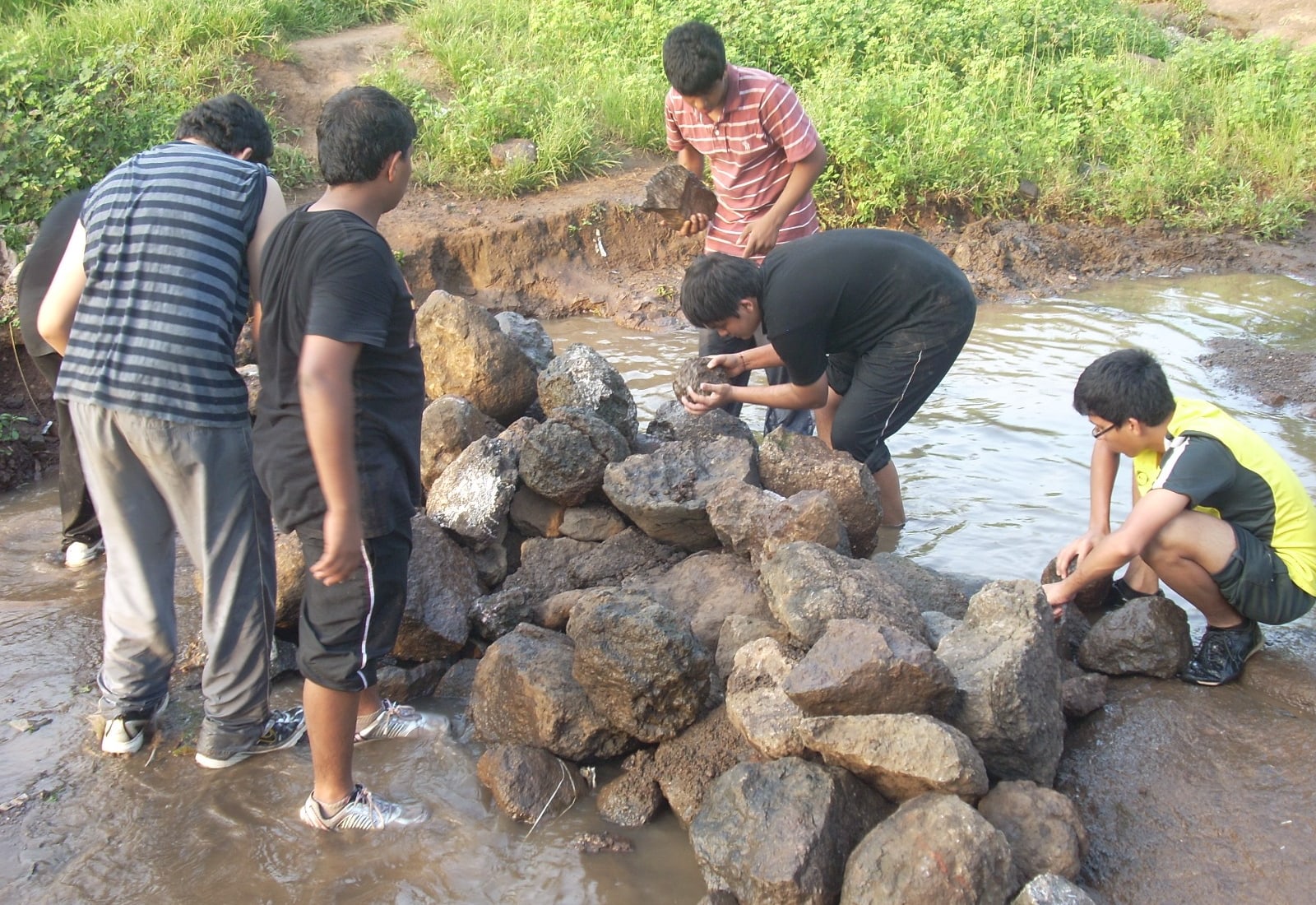 Students building a rock check dam in a village stream