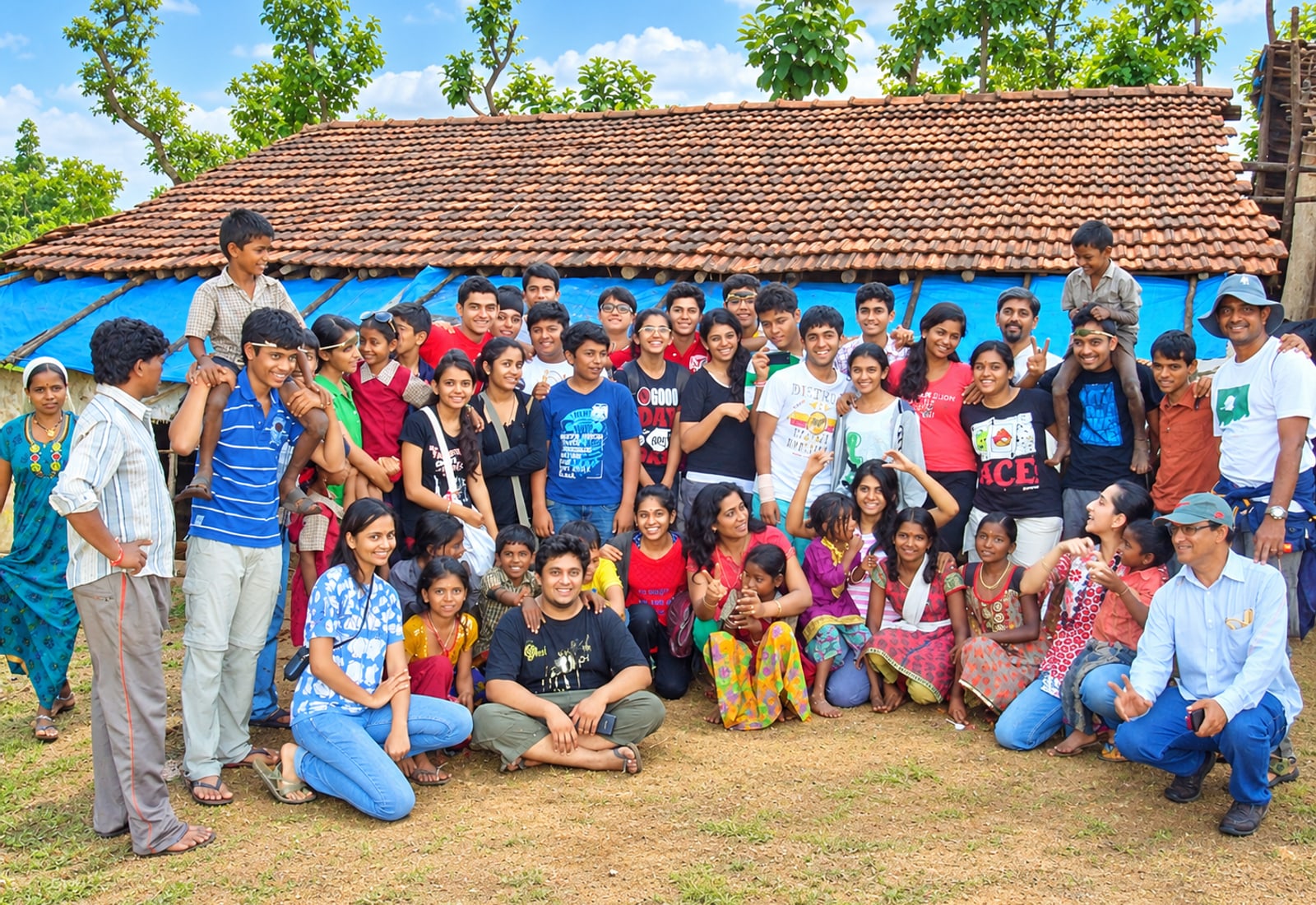 Students and a village community gathered outside a tiled-roof home